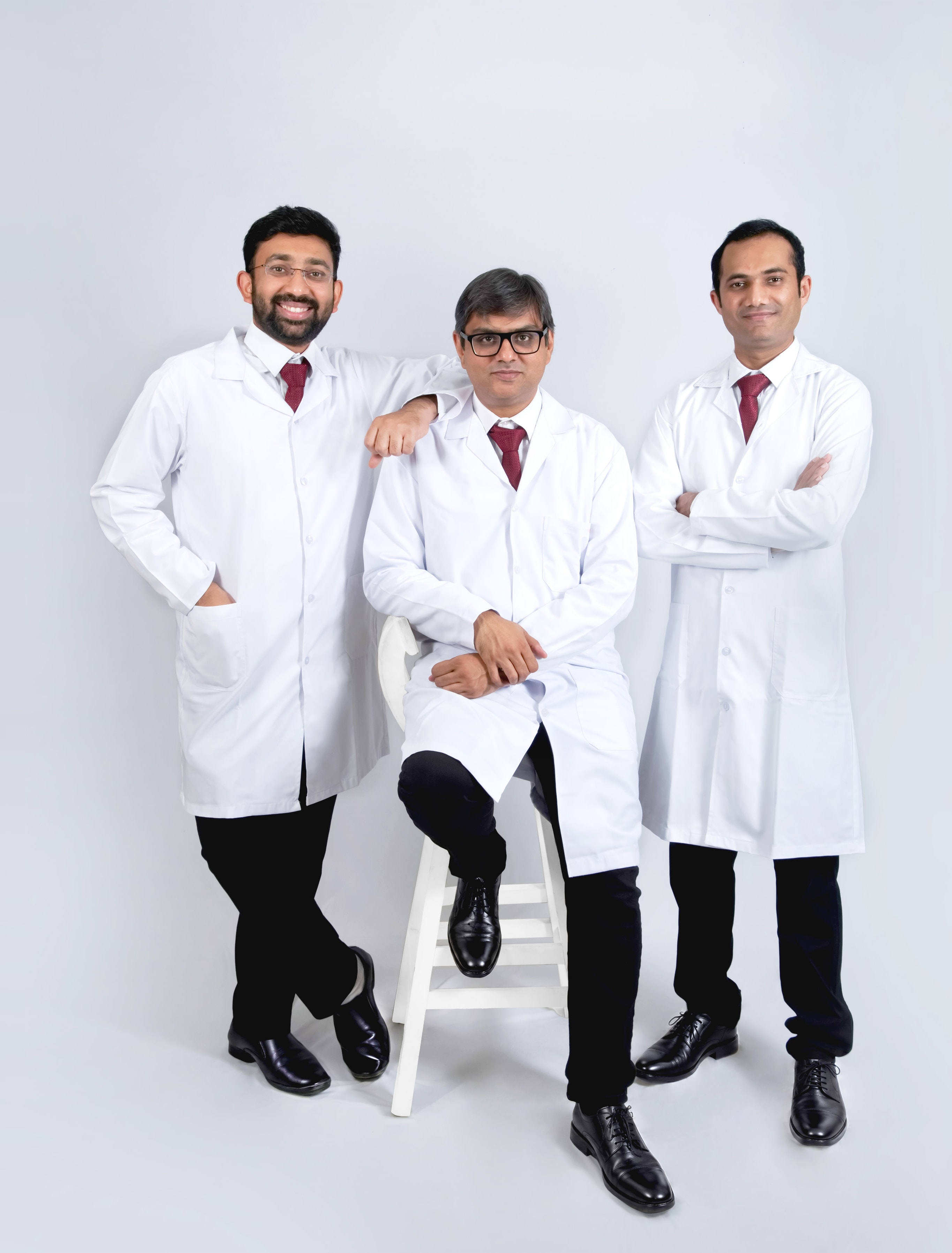The three founding oncosurgeons of Agastya Oncology, standing together in white coats